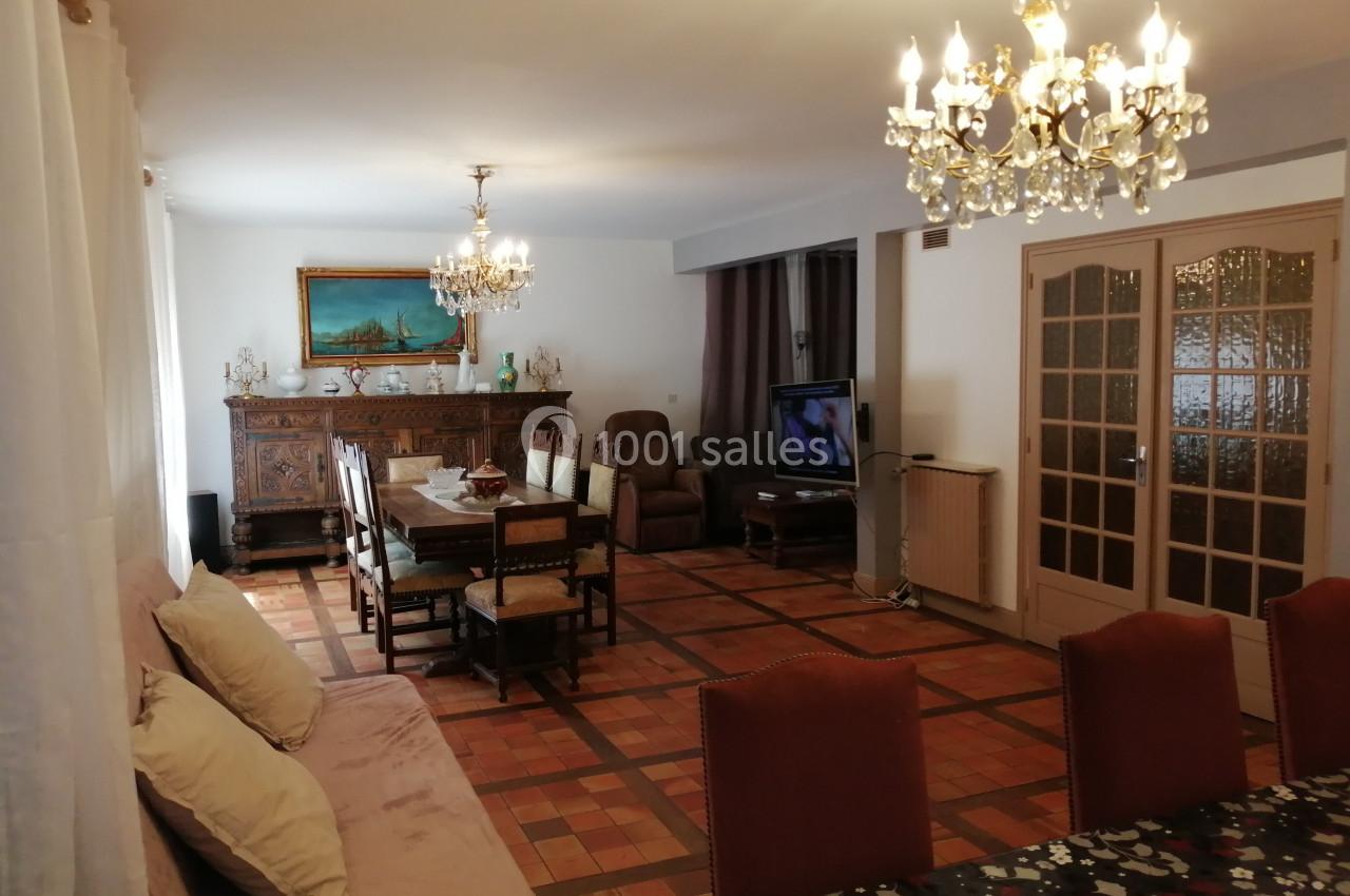 Salle à manger spacieuse avec table, chaises, canapé, buffet ancien, lustres et carrelage au sol.