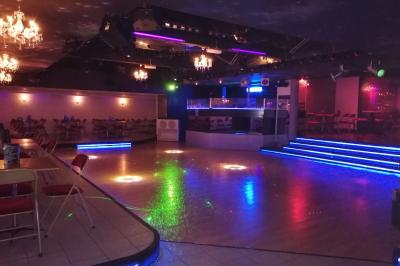 Salle de réception décorée avec des guirlandes et des lumières colorées, des invités assis et dansant.