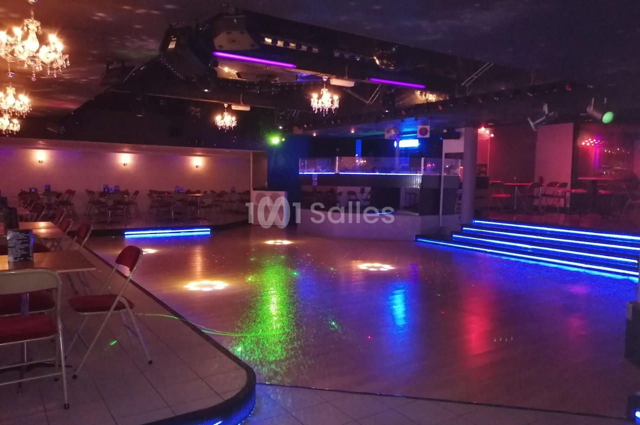 Salle de danse vide avec piste éclairée par des lumières colorées, tables et chaises disposées autour.