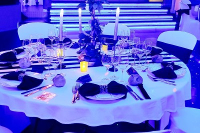 Salle de réception décorée avec des guirlandes et des lumières colorées, des invités assis et dansant.