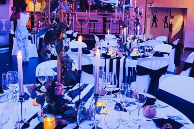 Salle de réception décorée avec des guirlandes et des lumières colorées, des invités assis et dansant.