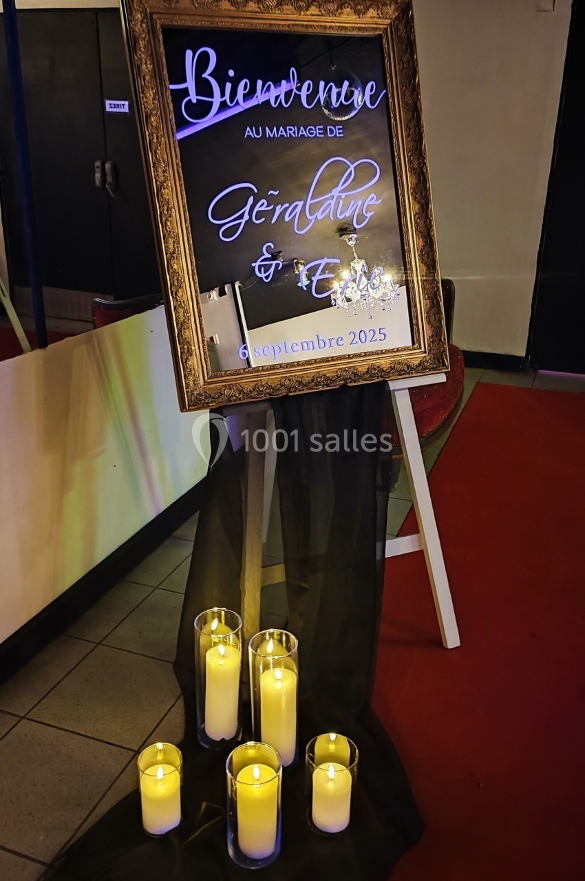 Panneau de bienvenue doré pour un mariage, entouré de bougies allumées et posé sur un chevalet avec un voile noir.
