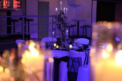 Salle de réception décorée avec des guirlandes et des lumières colorées, des invités assis et dansant.