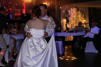Salle de réception décorée avec des guirlandes et des lumières colorées, des invités assis et dansant.