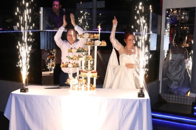 Salle de réception décorée avec des guirlandes et des lumières colorées, des invités assis et dansant.