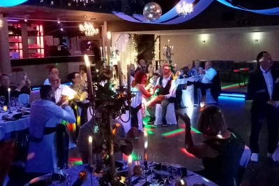 Salle de réception décorée avec des guirlandes et des lumières colorées, des invités assis et dansant.