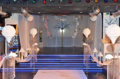 Salle de réception décorée avec des guirlandes et des lumières colorées, des invités assis et dansant.