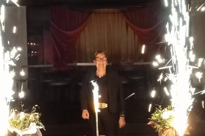 Salle de réception décorée avec des guirlandes et des lumières colorées, des invités assis et dansant.