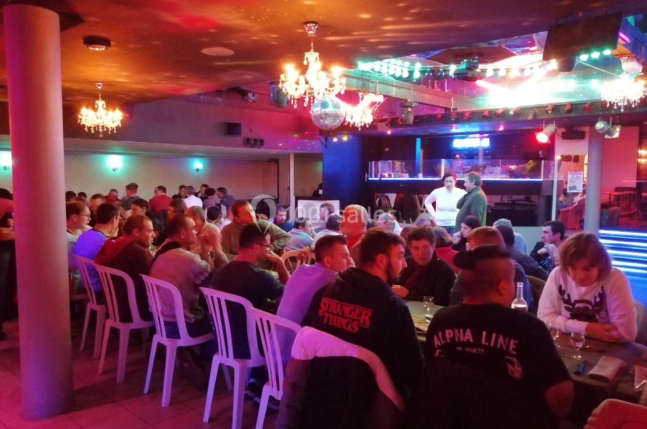 Salle remplie de personnes assises à des tables, éclairée par des lumières colorées et des lustres suspendus.