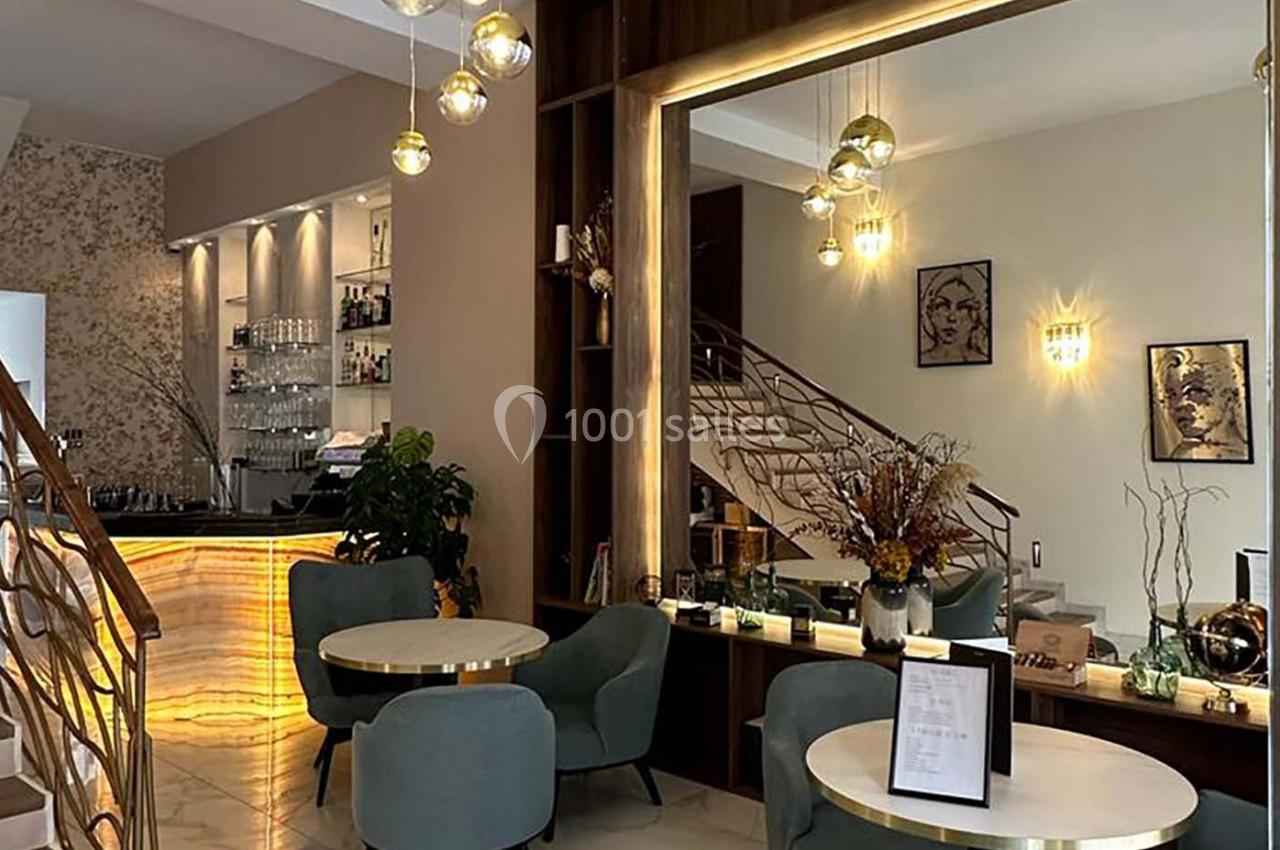 Intérieur d'un café moderne avec tables rondes, chaises rembourrées, grand miroir et comptoir lumineux.