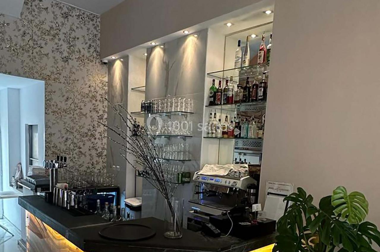 Bar moderne avec comptoir sombre, étagères de bouteilles, machine à café et décoration murale florale.