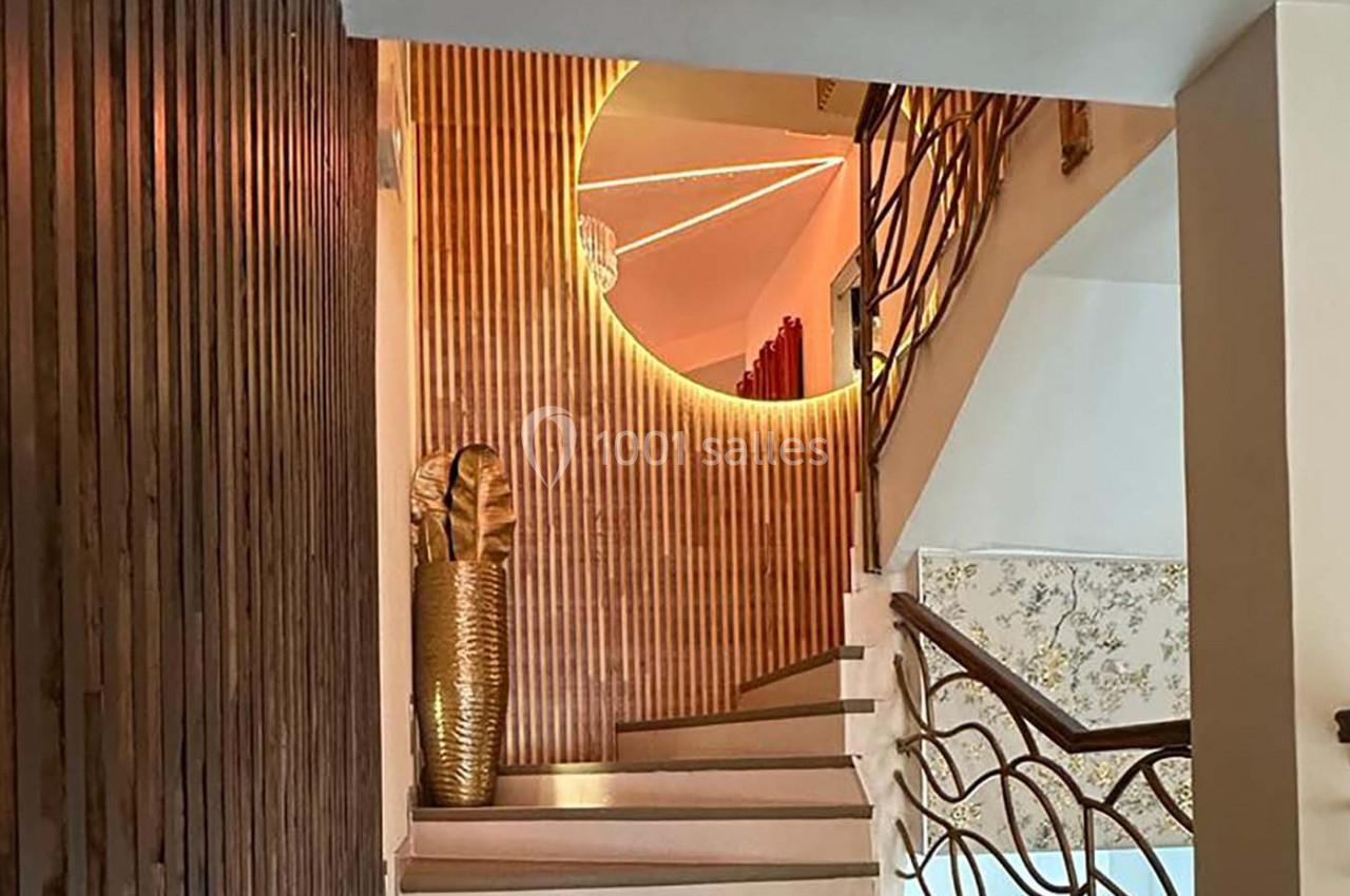 Escalier intérieur avec garde-corps en métal, mur en bois à lattes verticales et miroir rond éclairé.