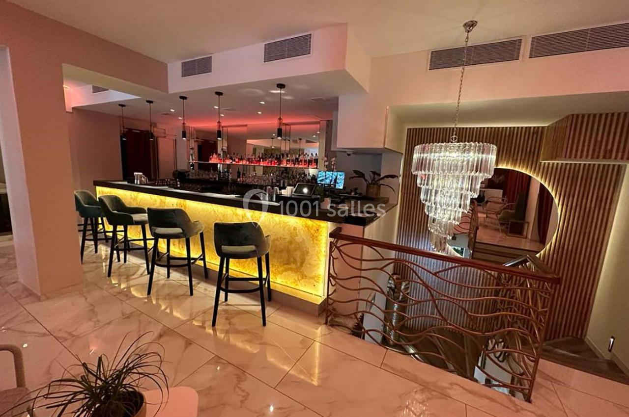Bar moderne avec comptoir éclairé, tabourets hauts, lustre en cristal et ambiance chaleureuse dans un espace élégant.