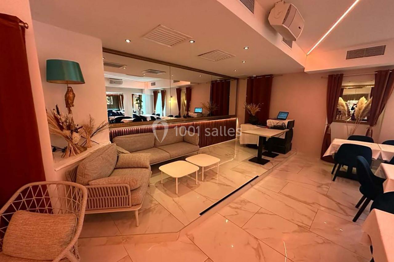 Salle lumineuse avec canapé, tables dressées, miroirs muraux et éclairage chaleureux.