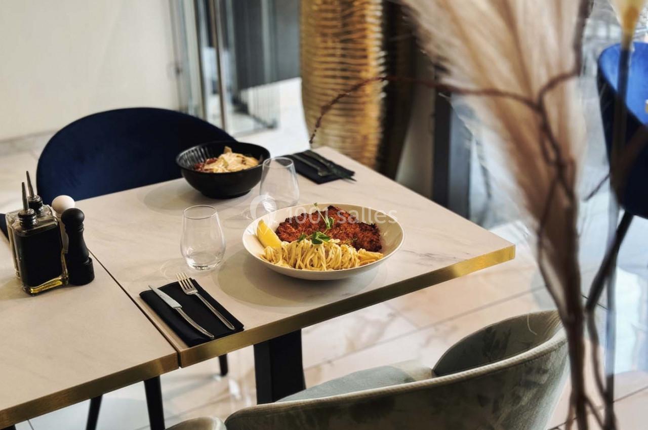 Assiette de pâtes avec escalope panée servie sur une table dressée dans un restaurant moderne et lumineux.