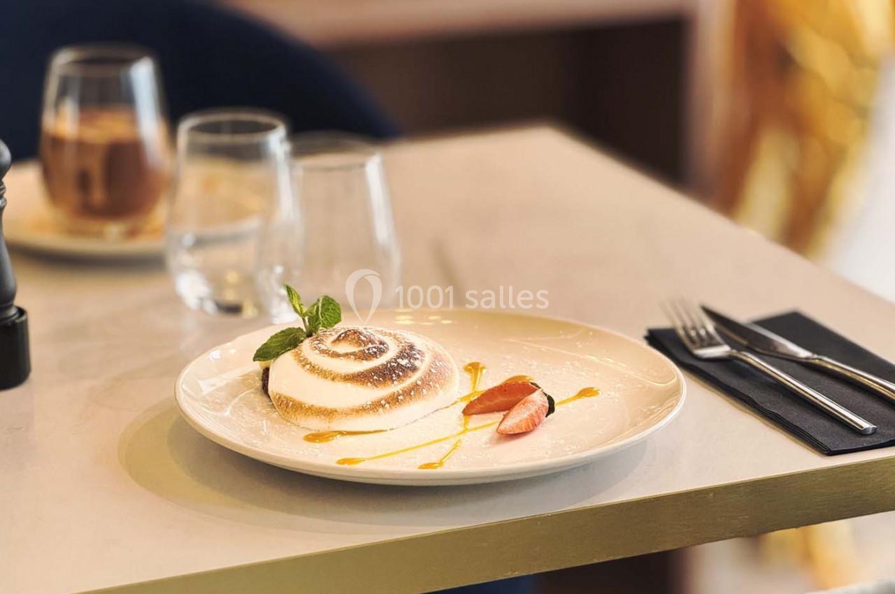 Dessert élégant présenté sur une assiette blanche, accompagné de coulis et de morceaux de fruits, sur une table dressée.