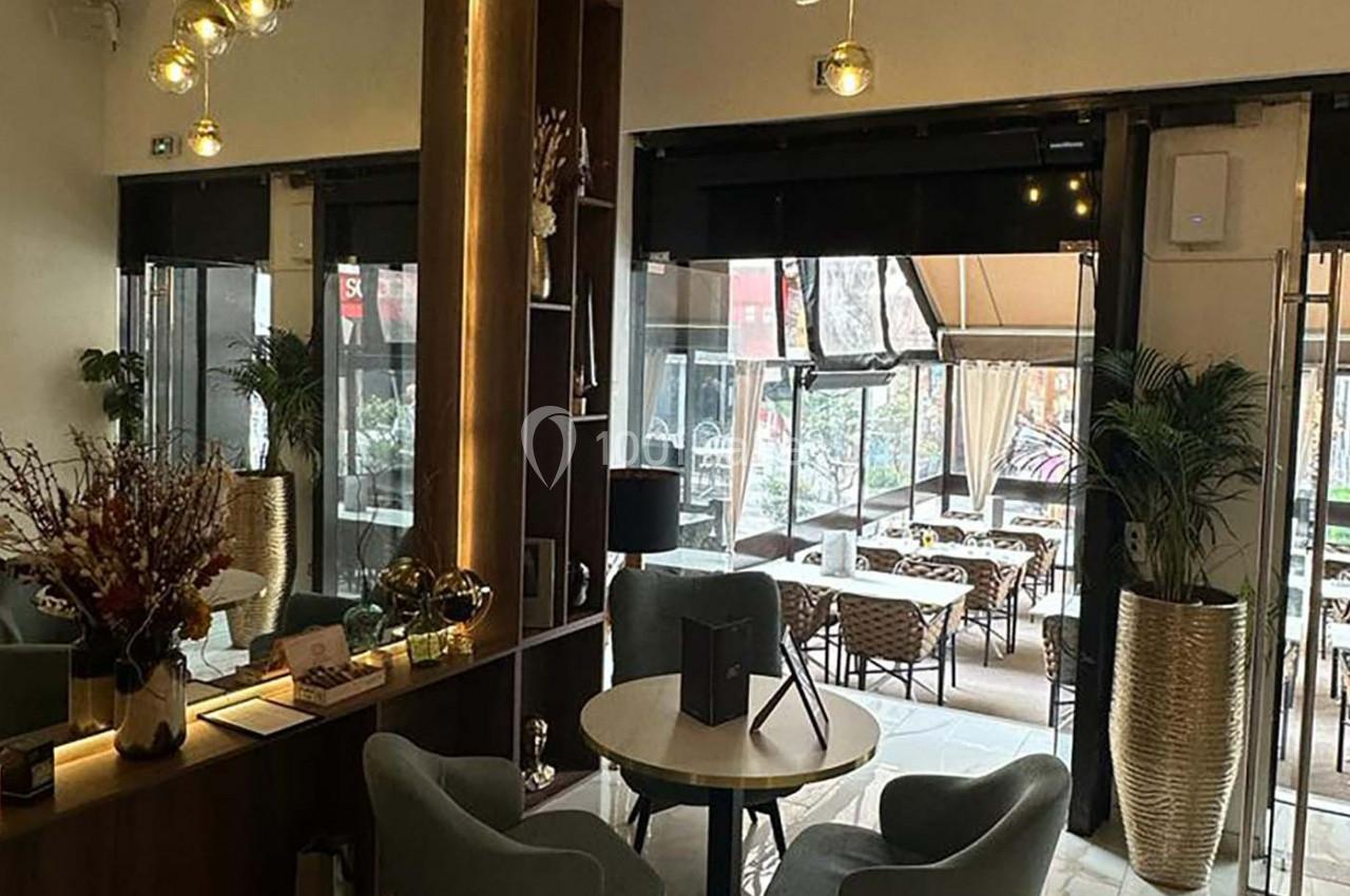 Intérieur d'un café moderne avec des fauteuils, des tables et une vue sur une terrasse extérieure aménagée.