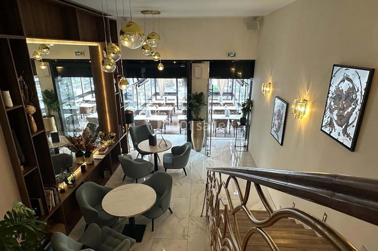 Espace intérieur élégant avec tables, fauteuils, luminaires modernes et vue sur une terrasse extérieure vitrée.