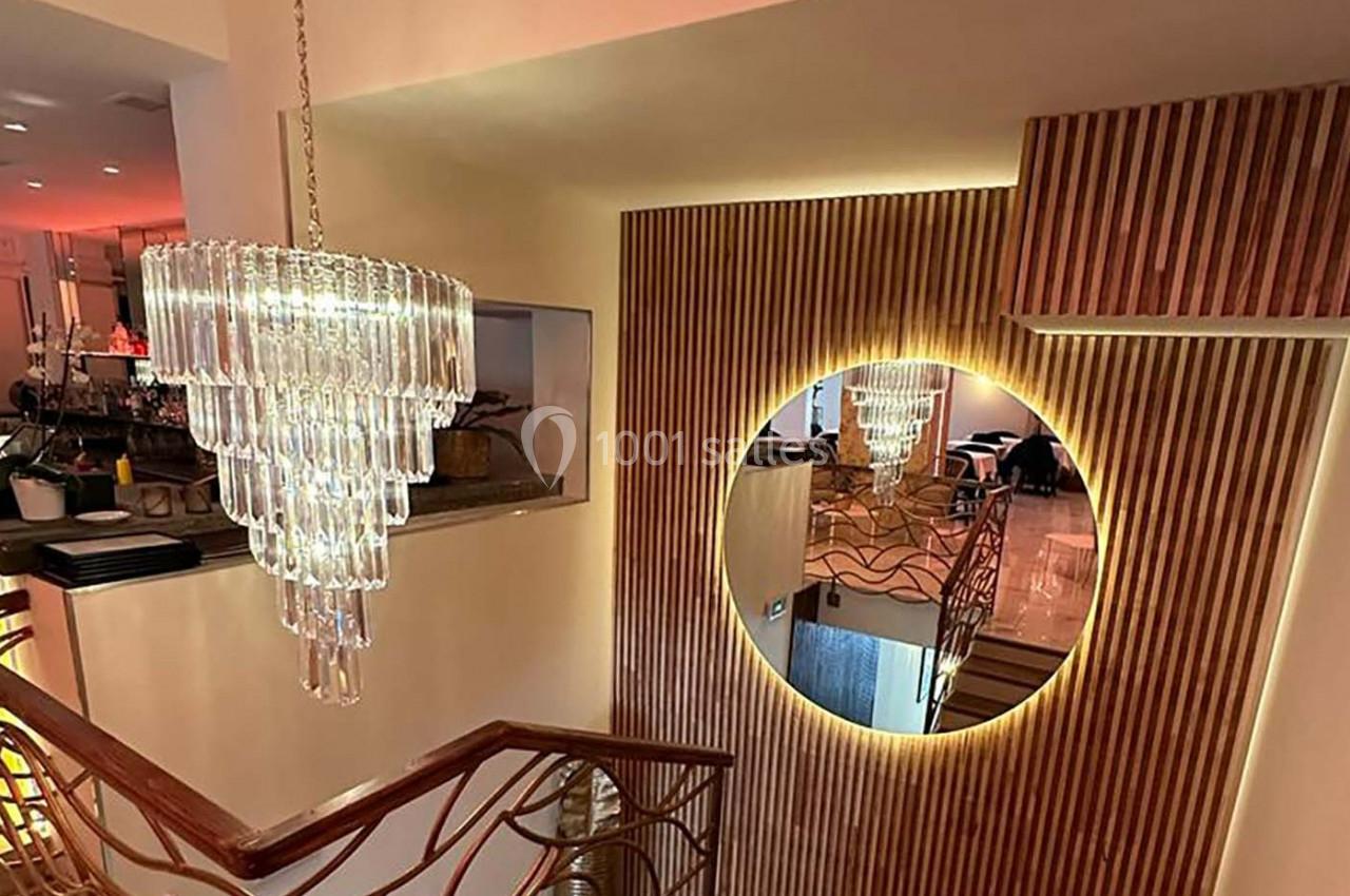 Lustre en verre suspendu près d'un escalier, avec un miroir rond encadré de bois et un éclairage chaleureux.