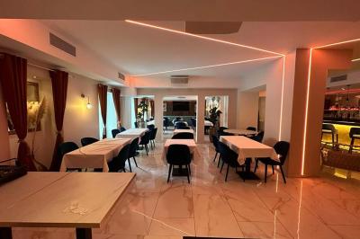 Salle de restaurant moderne avec tables dressées, chaises bleues, éclairage tamisé et bar illuminé en arrière-plan.