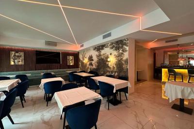 Salle de restaurant moderne avec tables dressées, chaises bleues, éclairage tamisé et bar illuminé en arrière-plan.