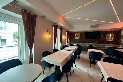 Salle de restaurant moderne avec tables dressées, chaises bleues, éclairage tamisé et bar illuminé en arrière-plan.