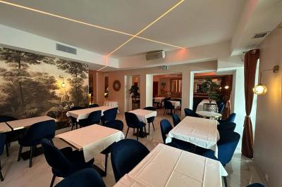 Salle de restaurant moderne avec tables dressées, chaises bleues, éclairage tamisé et bar illuminé en arrière-plan.