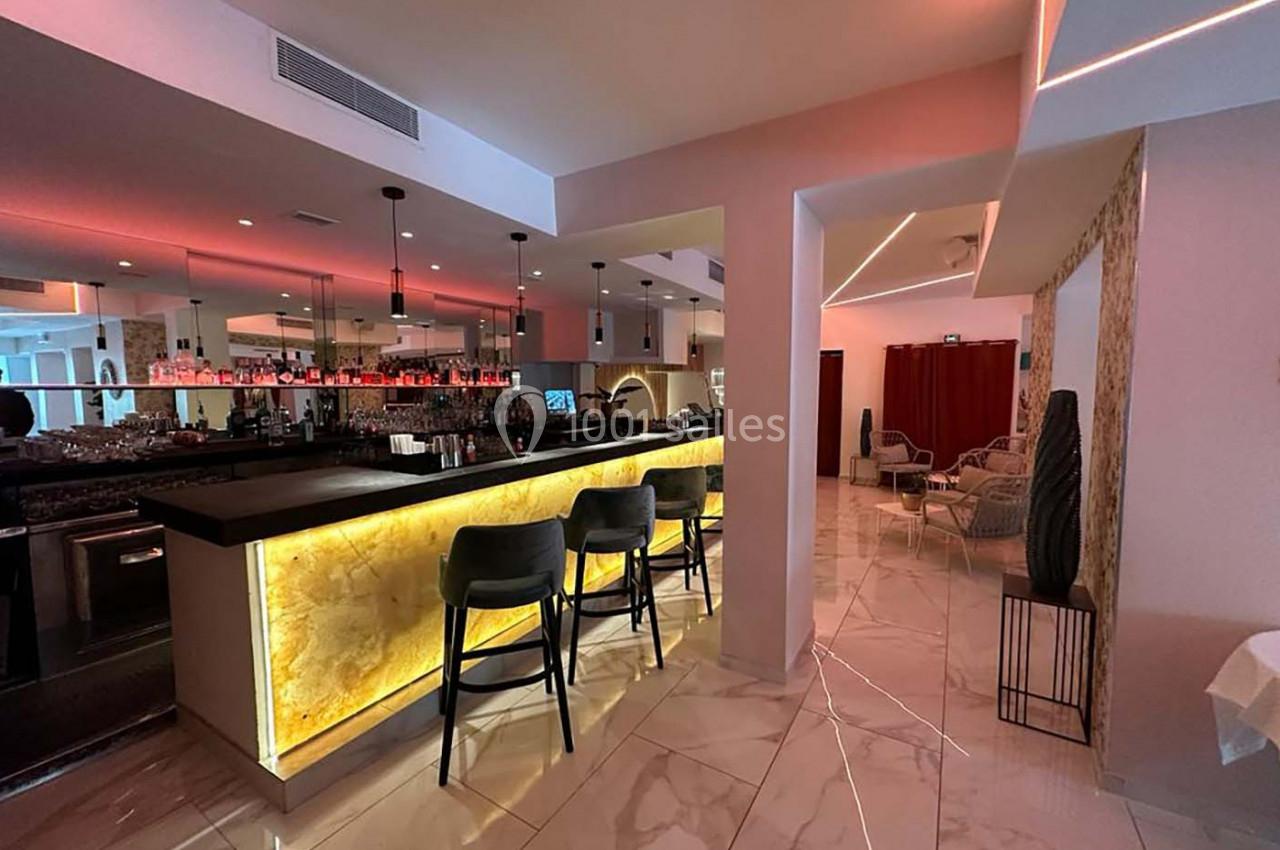 Bar moderne avec comptoir rétroéclairé en pierre, chaises hautes noires et ambiance lumineuse tamisée.