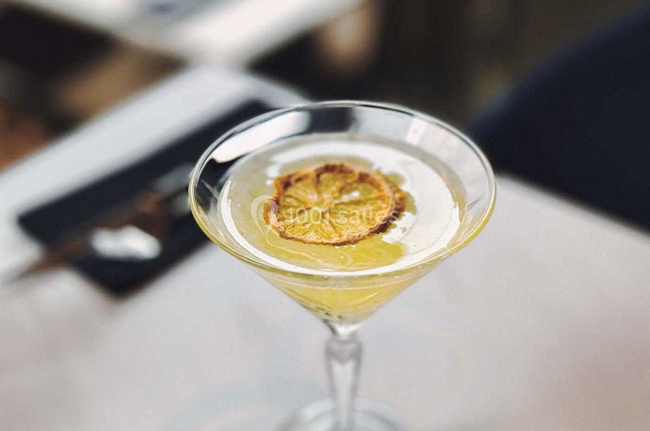 Verre à cocktail garni d'une tranche de citron séché, posé sur une table claire dans un environnement flou.