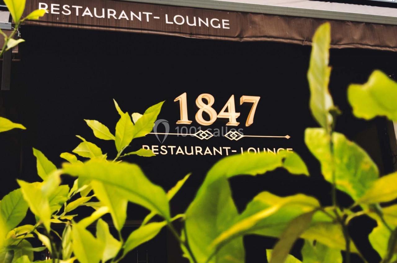 Façade d'un restaurant avec l'inscription ’1847 Restaurant-Lounge’, partiellement cachée par des feuilles vertes au premier…