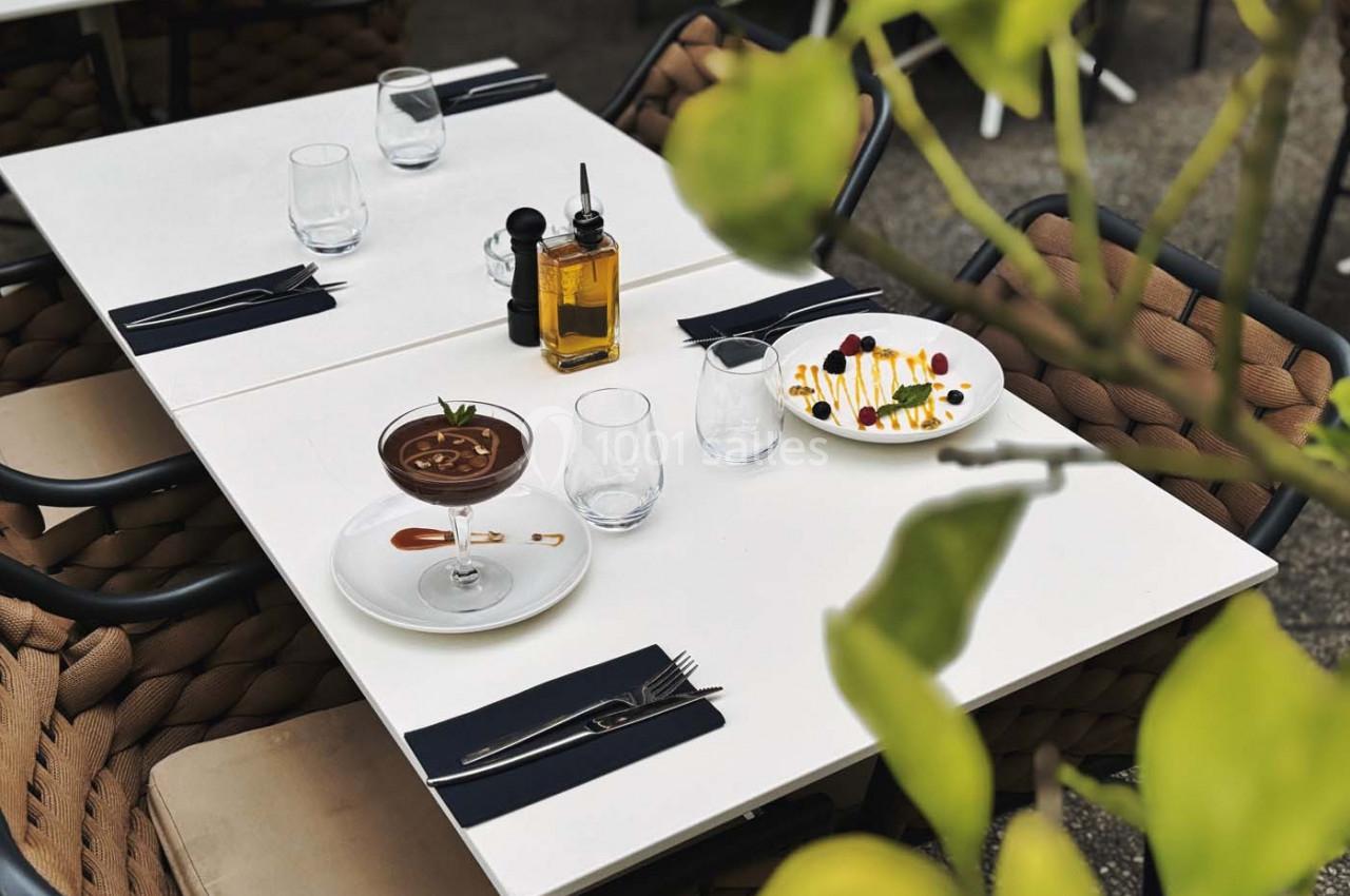 Table dressée en extérieur avec un dessert au chocolat, une assiette colorée, de l'huile d'olive et des verres vides.