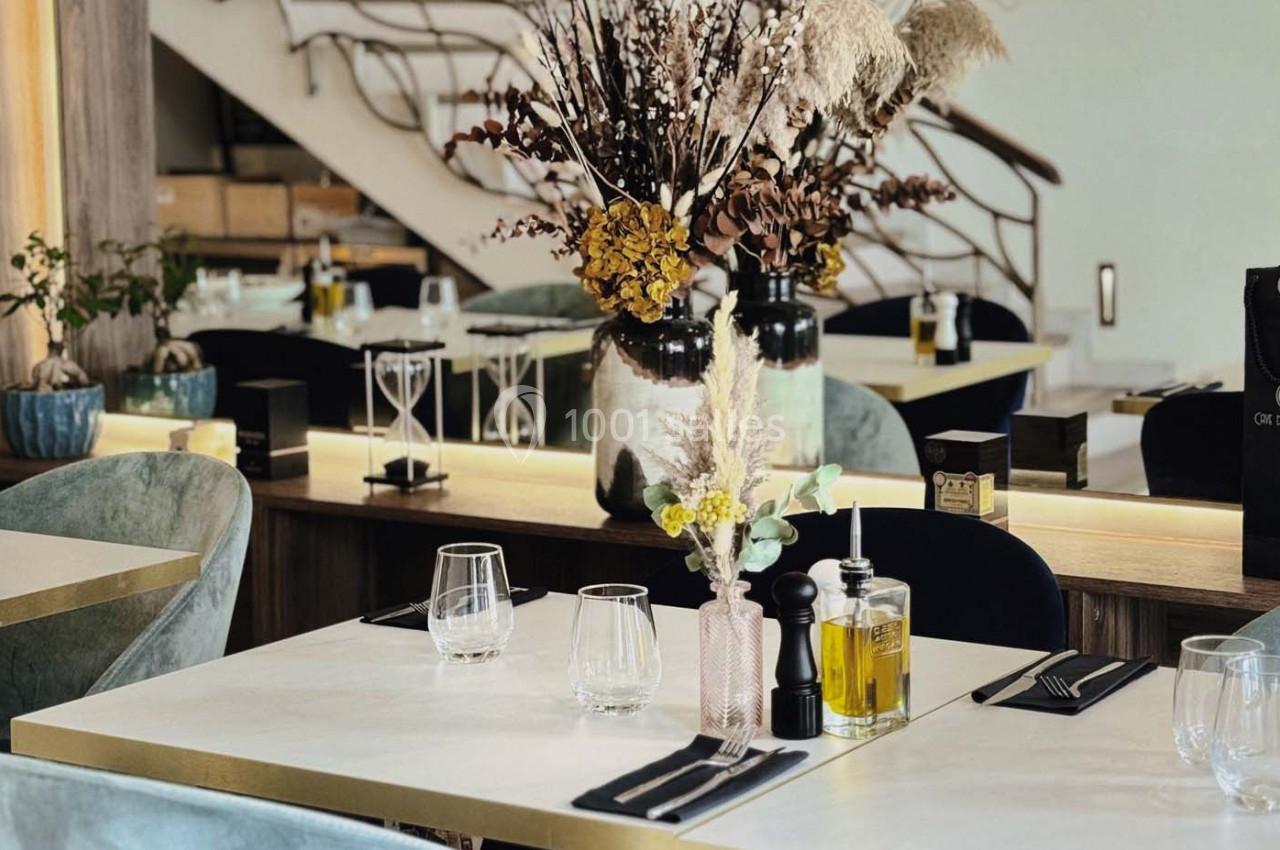 Table dressée dans un restaurant élégant avec décoration florale, chaises en velours et lumière naturelle.
