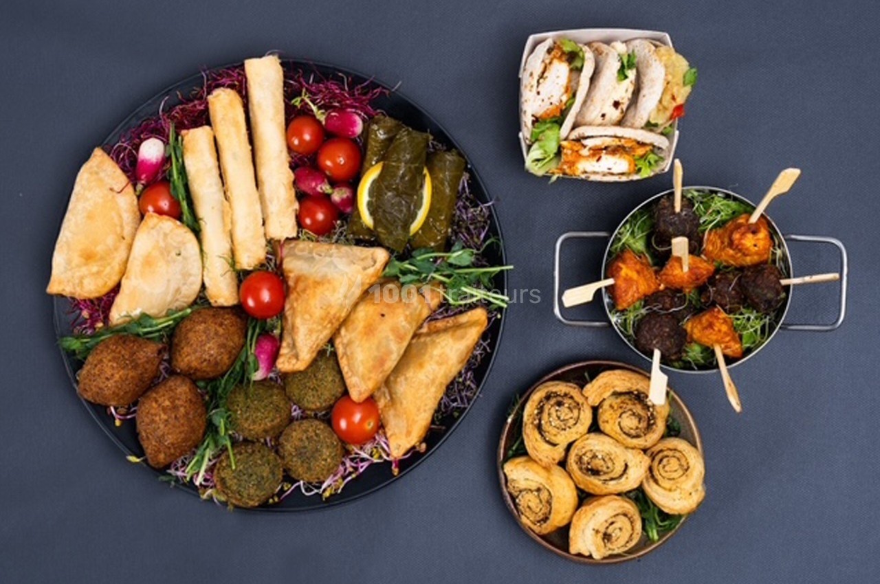 Assortiment de plats méditerranéens comprenant mezzés, feuilletés, falafels, wraps et légumes frais sur fond sombre.