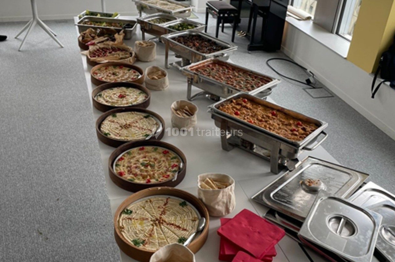 Buffet varié avec plats chauds en chafing dishes, tartes salées et accompagnements disposés sur une table blanche.