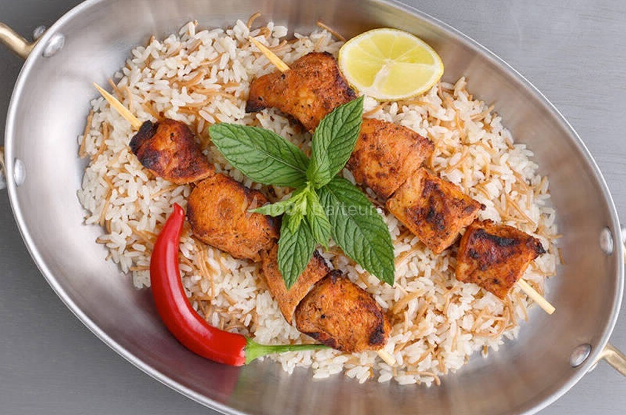 Brochettes de poulet grillé servies sur un lit de riz avec une rondelle de citron, un piment rouge et des feuilles de menthe.