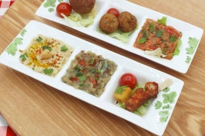 Assiette de wraps garnis autour d'un bol de sauce blanche, accompagnée de légumes marinés et de tranches de tomate.