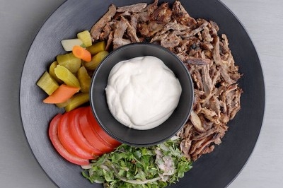 Assiette de wraps garnis autour d'un bol de sauce blanche, accompagnée de légumes marinés et de tranches de tomate.