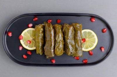 Assiette de wraps garnis autour d'un bol de sauce blanche, accompagnée de légumes marinés et de tranches de tomate.