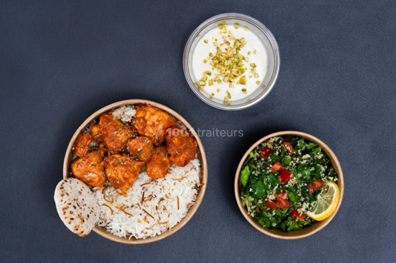Assiette de poulet épicé avec riz, pain plat, accompagnée d'une salade fraîche et d'une sauce au yaourt garnie de pistaches.