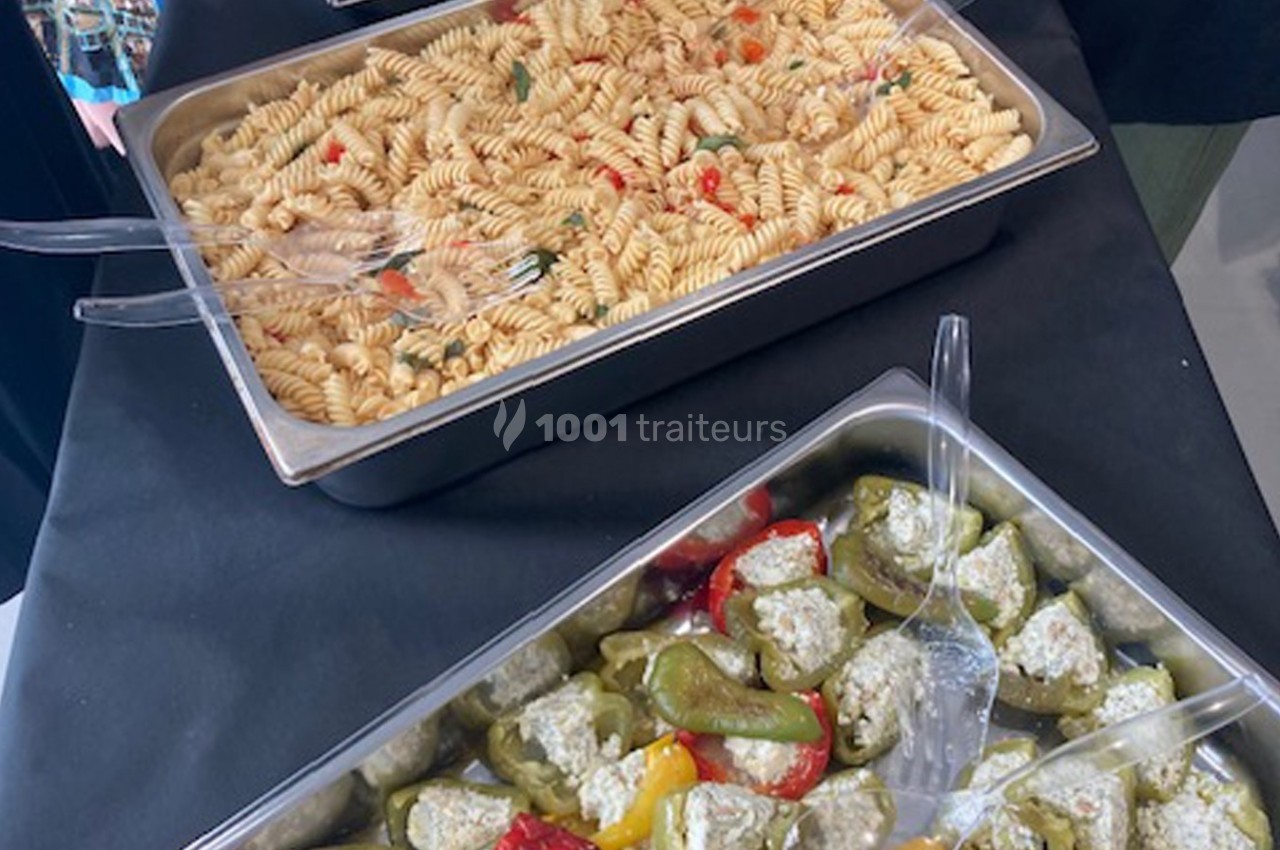 Plateaux de buffet contenant des pâtes aux légumes et des poivrons farcis au fromage, disposés sur une nappe noire.