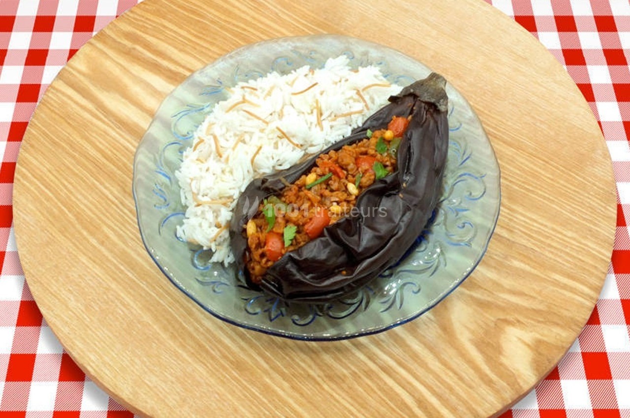 Aubergine farcie garnie de légumes et riz blanc servie dans une assiette sur une table en bois avec nappe à carreaux rouges.