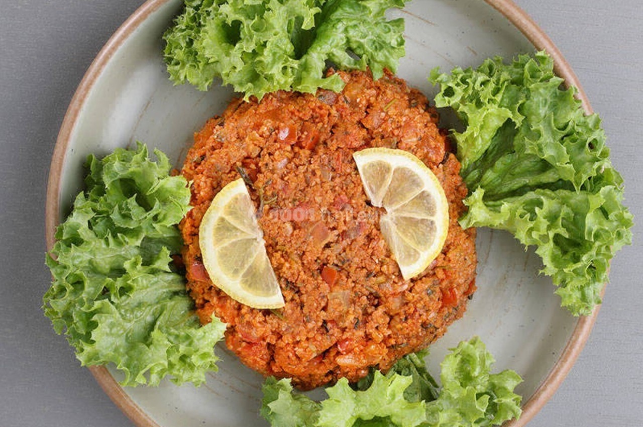 Assiette contenant un tartare végétarien entouré de feuilles de laitue et garni de deux tranches de citron.