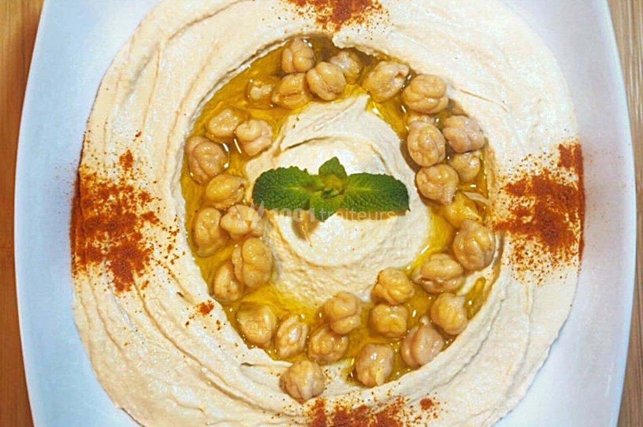 Assiette de houmous garni de pois chiches, huile d'olive, menthe et paprika, présentée sur une table en bois.