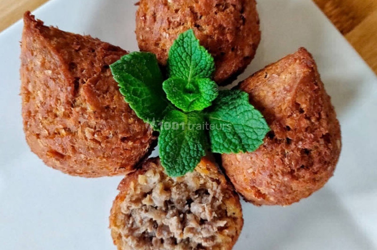 Quatre kibbeh dorés disposés en étoile sur une assiette blanche, garnis de feuilles de menthe fraîche.