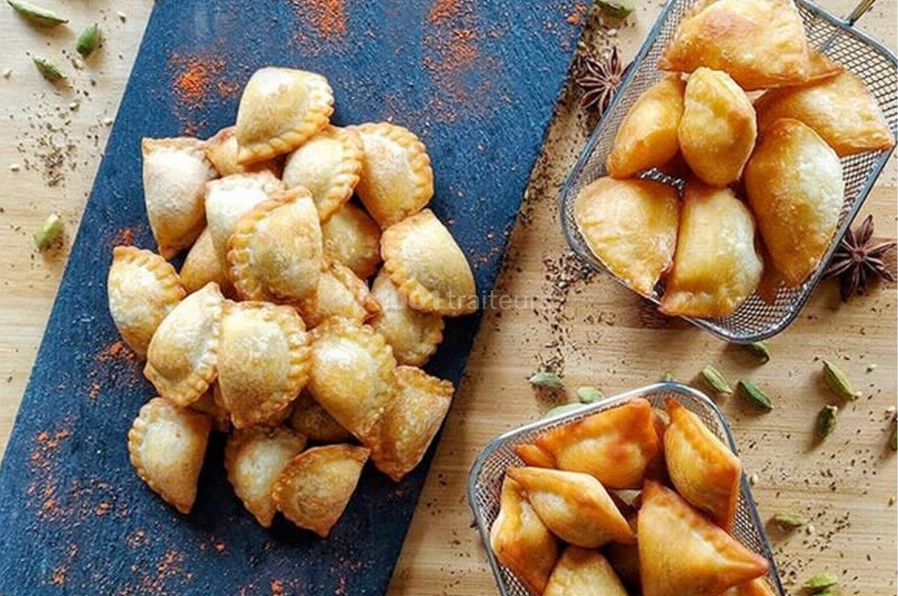 Assortiment de beignets dorés disposés sur une planche en ardoise et dans des paniers métalliques, entourés d'épices.