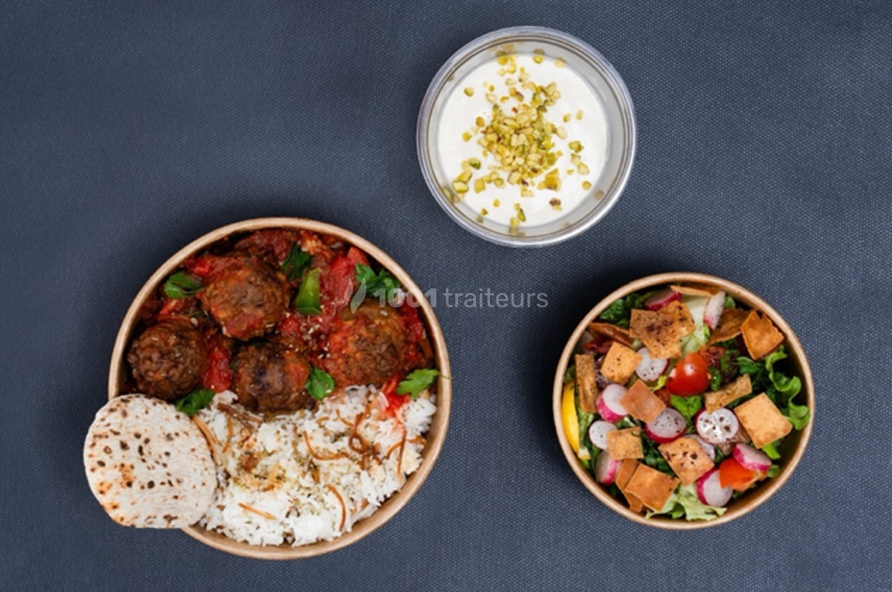 Assiette de boulettes avec riz et pain, accompagnée d'une salade colorée et d'un dessert au yaourt garni de pistaches.