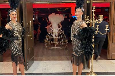 Entrée d'un bâtiment blanc entouré d'arbres, avec des portes vitrées illuminées par une lumière intérieure.