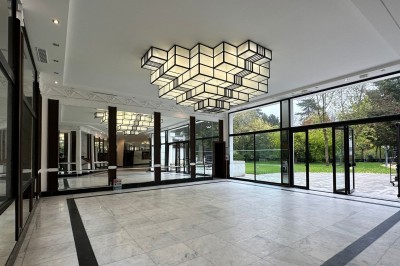 Entrée d'un bâtiment blanc entouré d'arbres, avec des portes vitrées illuminées par une lumière intérieure.