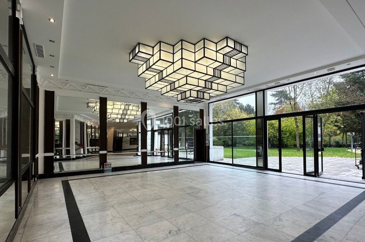 Hall spacieux avec sol en marbre, grandes baies vitrées donnant sur un jardin et un lustre géométrique suspendu.