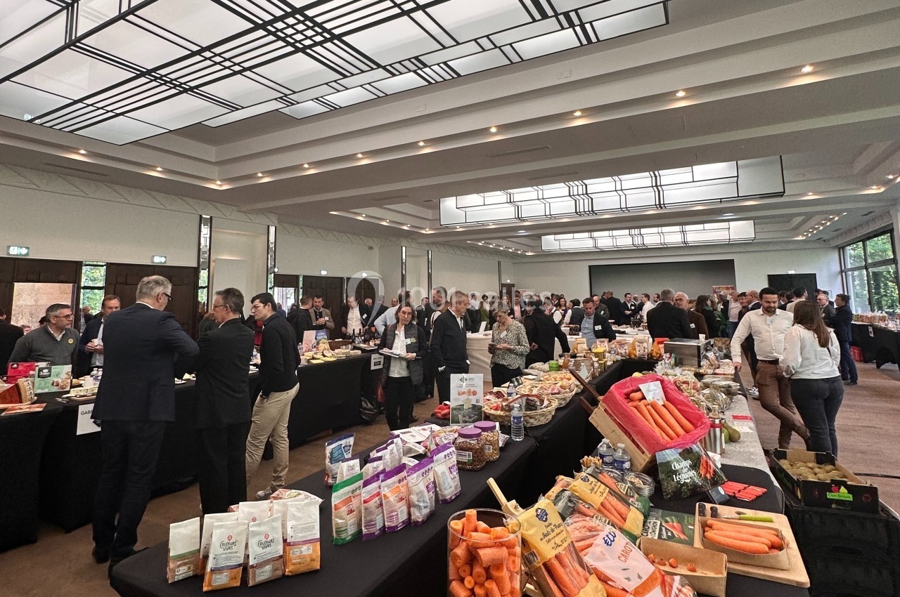 Salle de conférence avec des stands présentant des produits alimentaires, entourés de participants en discussion.